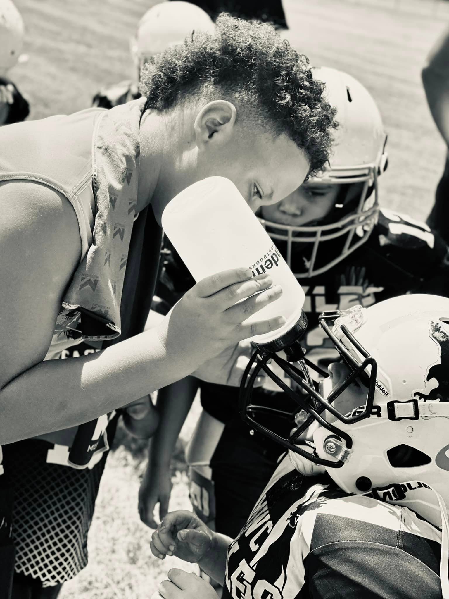 Image of boy providing water to players during a football game.